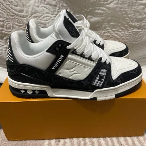 Louis Vuitton svartvita sneakers - Säljer ett par Louis Vuitton sneakers i svart och vitt med klassiskt monogrammönster. Skorna har snörning, platt sula och detaljer i skinn och textil. Ikoniska LV-detaljer på sidorna och sulan. Kommer med originalkartong och dustbags.