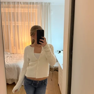 Crémevit kofta från Gina Tricot - Supermjuk och mysig crémevit kofta från Gina Tricot i stickat material. Koftan är croppad med rund halsringning och knäppning framtill med små knappar. Perfekt till jeans eller kjol för en chill look.