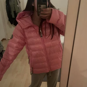 Rosa pufferjacka från C.A.Y.A - Säljer en rosa pufferjacka från C.A.Y.A med glansig finish och coola detaljer. Jackan har huva, dragkedjor framtill och på fickorna samt patch på ärmen. Perfekt för dig som vill sticka ut med en färgglad och trendig jacka! Bruker til vanlig small men passer meg som har jakken i medium. Helt ny selges pga jeg har fått en annen 