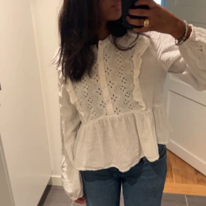 Vit blus med spets och volang - Säljer en söt vit blus med broderade spetsdetaljer och volanger längs bröstet. Knappt använd, från Bikbok. 