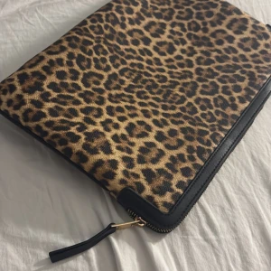 Leopardmönstrad datorväska med dragkedja - Säljer en snygg datorväska med leopardmönster i bruna och svarta toner. Väskan har en dragkedja runt om och detaljer i svart, perfekt för att bära din laptop med stil. Materialet är skinnimitation och insidan är helsvart.