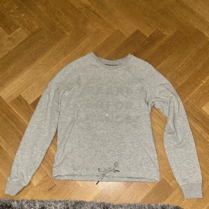 Grå sweatshirt Peak Performance XS - Säljer en grå sweatshirt från Peak Performance i storlek XS. Tröjan har tryckt logga framtill, långa ärmar och ribbade muddar. Nedtill finns en snörning för justerbar passform. Perfekt för en chill och sportig stil.