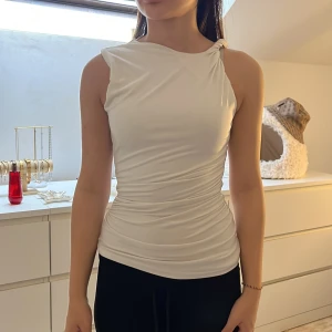 Vit topp - Säljer en vit, figurnära linnetopp med snygg omlott-effekt och knyt på ena axeln. 