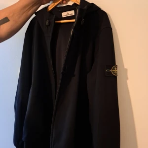 Svart vindjacka från Stone Island - Svart vindjacka från Stone Island. Klassisk logotyp-patch på vänster ärm. I stort sätt ny utan prislapp!