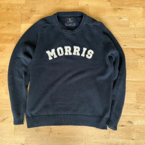 Mörkblå stickad tröja från Morris - Säljer en mörkblå stickad tröja från Morris med vit broderad text på bröstet. Tröjan har rund halsringning och långa ärmar. Perfekt för dig som gillar klassisk och stilren design. Väldigt fint skick!