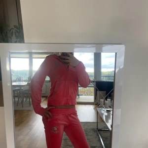 Rosa Juicy Couture hoodie  och byxor till med glitter - Säljer en ikonisk rosa hoodie och byxorna från Juicy Couture med glittrigt silvertryck på bröstet och ryggen. Tröjan har huva, dragkedja och två fickor framtill. Mjuk velourkänsla och klassisk passform, perfekt för dig som gillar den Y2K-stilen. Säljer byxor till så ett sätt💗 har dock en svart lite fläck på fram sidan av tröjan! Köpte byxorna för 800kr och tröjan för 900kr
