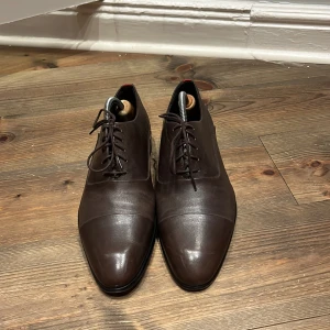 Hugo boss skor  -   Säljer ett par stilrena herrskor från Hugo Boss, tillverkade i äkta läder med högkvalitativ finish. Skorna är bruna i en tidlös design som passar lika bra till kostym som till ett mer avslappnat business casual-utseende.