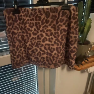 Leopardmönstrad kjol från SHEIN - Säljer en snygg kortkjol från SHEIN med leopardmönster i bruna och beige toner. Kjolen är i polyester och har en rak passform som ger en cool vibe. Perfekt för dig som vill sticka ut med ett djurmönster i garderoben. Med inbyggda shorts