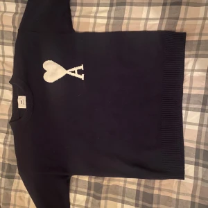 Marinblå stickad tröja från Ami Paris - Marinblå stickad tröja från Ami Paris med vit hjärtlogga och bokstaven A på bröstet. Klassisk rund halsringning och ribbade muddar. Perfekt för dig som gillar stilrena och trendiga plagg med en twist.  Säljer för att den är för stor. Använd några gånger men aldrig tvättad. Pris kan självklart diskuteras 