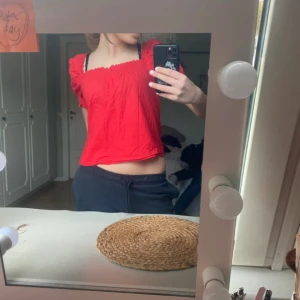 Röd smockad blus från H&M - Röd blus från H&M med smockad överdel och ärmslut. Modellen är croppad med korta puffärmar och rynkade detaljer. Perfekt för dig som gillar färg och vill ha en luftig topp med söt vibe.