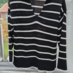 Svartvitrandig stickad tröja från Amisu - Svart stickad tröja från Amisu med vita horisontella ränder, v-ringning och krage. Tröjan har långa ärmar och ribbade muddar med vit kant. Perfekt för dig som gillar en chill och stilren look.sprund i sidan djur o rökfritt hem.
