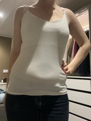 Vit linnetopp  - Säljer en enkel och stilren vit linnetopp med smala axelband. Toppen är ärmlös och har en tight passform som sitter snyggt mot kroppen. Perfekt för varma dagar eller som lager under andra plagg.