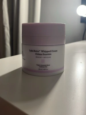 Drunk Elephant Lala Retro Whipped Cream - Lala Retro Whipped Cream från Drunk Elephant är en ansiktskräm med triple-ceramide blend och 5 afrikanska oljor. Kommer i en rund, ljuslila plastburk med pumpfunktion, 50 ml. Perfekt för dig som vill ha en återfuktande och lyxig känsla i din hudvårdsrutin.