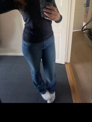 Blå bootcut jeans med midwaist - Säljer ett par snygga blå bootcut jeans med klassisk femficksdesign och midwaist. Jeansen har en lätt tvättad look och är tillverkade i mjukt jeansmaterial som sitter skönt. Passformen är normal och benen är utsvängda nedtill för en trendig siluett.