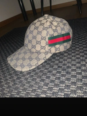 Fet keps - Bilderna visar en keps.. Kepsen har klassiskt GG-mönster och grönt/rött band på sidan.