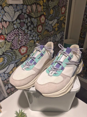 Diadora Terrena Nylon Vibram sportskor Storlek 45 - Säljer ett par chunky Diadora sneakers med Vibram-sula. Skorna är vita och beige med detaljer i blått, lila och mintgrönt. Ovandelen är i mesh och mocka, med snörning och rund tå. Perfekt för dig som gillar retrostil och färgkombinationer.