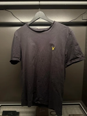 Svart t-shirt från Lyle & Scott M - En svart t-shirt från Lyle & Scott i storlek M. Klassisk modell med rund hals och korta ärmar. På bröstet sitter den ikoniska gula örnloggan broderad. Tillverkad i mjuk bomull för skön känsla och enkel stil.