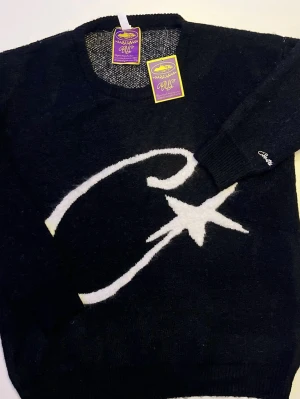 Svart stickad Cortiez tröja - Svart stickad tröja från MS med ett stort vitt stjärnmotiv och böjd linje på framsidan. Tröjan har rund halsringning, långa ärmar och ribbade muddar. Materialet är mjukt och passar perfekt för kyligare dagar.