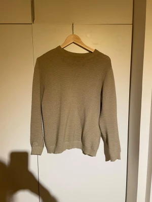Beige stickad tröja från Pull&Bear - Säljer en beige stickad tröja från Pull&Bear i storlek S. Tröjan har en rund halsringning, ribbade muddar och ett diskret ribbat mönster över hela plagget. 