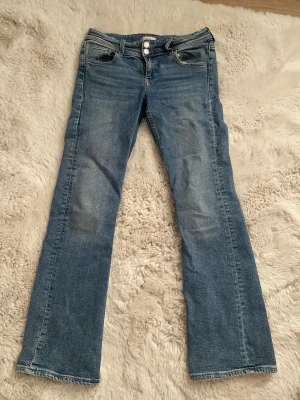 Blå bootcut jeans Gina Tricot 164 - Snygga blå jeans från Gina Tricot i storlek 164. Modellen har bootcut-ben, klassiska fem fickor och dubbla knappar framtill. Jeansen är tillverkade i ett mjukt bomullsmaterial och har en lätt tvättad look.