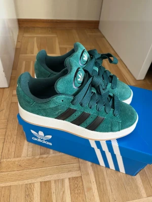 Adidas Campus gröna sneakers - Säljer ett par Adidas Campus sneakers i mörkgrön mocka med svarta ränder. Fick ett par i julklapp men tyvärr passa dom inte mig då jag har storlek 39 och detta är st 38! Har aldrig används, dom är helt nya och nypris ligger på 1300-400kr! Om du bor i Göteborg finns det möjlighet att hämta 