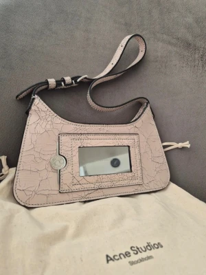 Rosa micro handväska från Acne Studios - Säljer en beige handväska från Acne Studios med sprucket mönster och justerbar axelrem. Fått i present men aldrig använt. Ny pris på nätet 8000:-. 