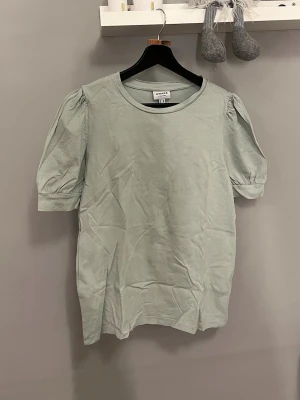 Ljusgrön blus från AWARE Vero Moda - Säljer en ljusgrön blus från AWARE by Vero Moda i storlek M. Blusen har puffiga korta ärmar och rund halsringning. Tillverkad i mjuk bomull, perfekt för dig som gillar enkel och stilren design med en liten twist på ärmarna.