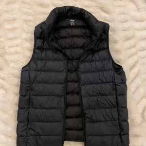 Marin blå väst från Uniqlo - Svart dunväst från Uniqlo med quiltad design och hög krage. Västen har en stilren look med horisontella sömmar och dragkedja framtill. Perfekt att slänga över en hoodie eller tröja när det är kyligt ute. Lätt och smidig att bära med sig.