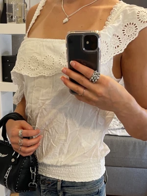 Vit offsholder blus - Superfin vit blus med one off shoulder, broderad volang upptill och smockad nederkant. Passar XS/S.