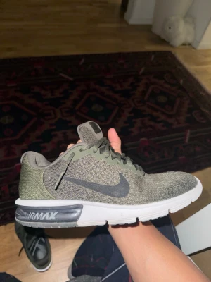 Nike Air Max sneakers i olivgrönt - Nike Air Max sneakers i olivgrön och grå färg med stickad ovandel och klassisk Air Max-sula. Skorna har snörning, rund tå och vit platt sula med synlig Air Max-dämpning. Perfekt för dig som gillar sportig stil och bekväma skor.