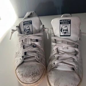 Adidas Stan Smith vita sneakers 37 1/3 - Klassiska vita Adidas Stan Smith sneakers med snörning och rund tå. Skorna är i skinn och har diskreta perforerade ränder på sidorna samt logga på plösen och hälen. Perfekta för en clean och tidlös stil.