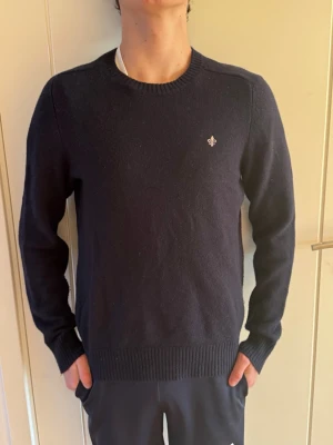 Mörkblå stickad tröja Morris S - Snygg mörkblå stickad tröja från Morris i storlek S i merino ull. Tröjan har rund hals, ribbade muddar och en liten broderad logga på bröstet. Perfekt för dig som gillar klassisk stil med en modern touch.