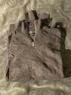 Grå grön half zip tröja Jack & Jones - Snygg grå tröja från Jack & Jones med half zip och hög krage. Tröjan är stickad i mjukt material och har ribbade muddar vid hals och ärmslut. Perfekt för dig som gillar enkel och stilren design.