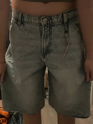 Ljusblå denimbermuda från FB Sister - Säljer ett par ljusblå, loose fit denimbermuda från FB Sister. De har hög midja, råa kanter nertill och klassiska femficksdetaljer. Perfekta för en chill och avslappnad stil. Materialet är bomull och de har dragkedja och knapp framtill.