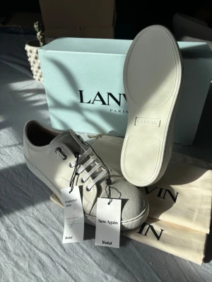Lanvin cap toe - Snygga vita sneakers från Lanvin i lyxigt kalvskinn med unik grå textur på tån. Klassisk låg modell med rund tå, vita snören och diskret logga på sulan. Kommer med originalkartong och dustbag. Perfekta för dig som gillar stilrena och exklusiva sneakers. *dessa är limited edition, helt oanvända och säljs ej mer, dem sitter som 42,5-43 och är äkthetsverifierade av vinted! Nypris är över 5000kr.