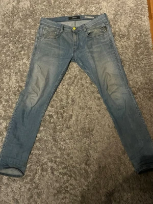 Replay ljusblå slim fit  - Säljer ett par ljusblå Replay jeans med skinny passform och klassisk femficksdesign. Jeansen har en gul knapp framtill och tydliga Replay-loggor på bakfickorna. Materialet är stretchigt jeans och de har en snygg tvättad look.
