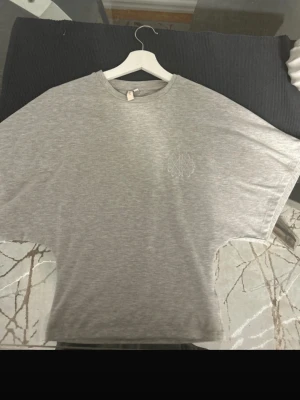 Round Neck Wide Sleeve Tee Nelly - Säljer en grå t-shirt från Nelly i storlek XXS. T-shirten har korta ärmar, rund hals och ett diskret tryck på bröstet. Materialet är mjuk bomull som känns skönt mot huden. Perfekt för dig som gillar enkel och clean stil. Tight åt midjan som ger en fin figur.