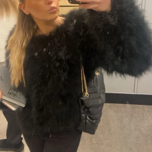 Svart jacka från Hollies - Säljer en svart pälsjacka från Hollies i äkta fjäder. Den är helsvart, har lång ärm och en oversized look. Fodrad insida för extra komfort. Superfin! 