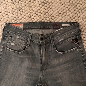 Replay Anbass grå jeans herr - Snygga Replay Anbass jeans i grå tvätt med slitningar och klassiska fem fickor, perfekt till sneakers eller boots. Tydlig Replay-logga på fickan och diskreta detaljer. Jeansen är i stretchigt denim för extra komfort.