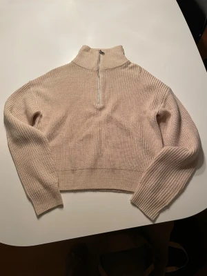 Beige stickad half zip-tröja Bik Bok - Säljer en beige stickad tröja från Bik Bok i storlek XS. Tröjan har en hög krage med half zip-dragkedja framtill och är ribbstickad med långa ärmar. Perfekt för dig som gillar en enkel men snygg look.