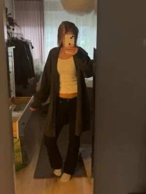 Mörkgrå lång kofta - Säljer en lång och mysig mörkgrå kofta med lös passform. Koftan är stickad och har långa ärmar, perfekt att slänga på sig över en topp eller t-shirt. Enkel och stilren design som passar till många outfits.