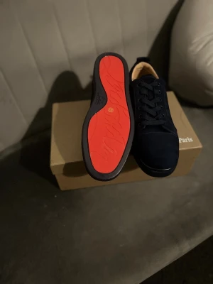 Louboutins - Säljer ett par mörkblå sneakers från Christian Louboutin med klassisk röd sula och snygg snörning. Skorna är tillverkade i mocka och har rund tå samt platt sula. Kommer med originalkartong och tillbehör. Perfekta för dig som vill sticka ut med exklusiv stil. Behöver bli av med dem kom med prisförslag