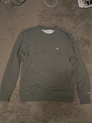 Calvin Klein sweatshirt - En grå Calvin Klein sweatshirt (herrmodell). Säljs då den inte används. Använd ett fåtal gånger. 