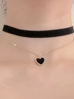 Svart sammet choker med hjärthänge - Snygg svart choker i sammet med ett tunt kedjehalsband och ett hjärthänge i svart och guld. Chokern har ett klassiskt, brett band och hjärtat är ca 1,4 cm högt. Perfekt accessoar för att ge din outfit en cool och trendig vibe.