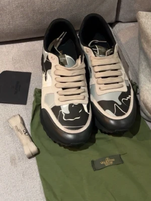 Valentino Rockrunner sneakers i svart och grått - Säljer ett par Valentino Rockrunner sneakers med svart, grått och vitt camouflage-mönster. Skorna har rund tå, platt sula och snörning. Materialet är en mix av skinn och textil. Snygga detaljer och ikonisk design från Valentino.