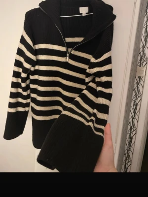 Svartvit randig stickad hoodie H&M XS - Säljer en svart och vit randig stickad hoodie från H&M i storlek XS. Tröjan har huva, lång ärm och half zip framtill. Ribbad struktur och breda muddar ger en chill och snygg look. Perfekt för dig som gillar streetstyle och vill ha något varmt och mjukt.