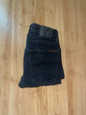 Nudie Jeans  - Säljer ett par mörkblå Nudie Jeans, Tube Tom. Jeansen har en slim passform och är tillverkade i stretchig bomull för extra komfort. Midja 31cm, längd 88cm. JAG SKICKAR EJ FLER BILDER NÄR JAG BÄR JEANSEN! för bättre inblick i passformen rekommenderar jag att googla på modellnamnet. För storleksguide kolla måtten noggrant då jeansen alltid kan vara uppsydda heller krympta och jag ej tar emot returer :) s5,3