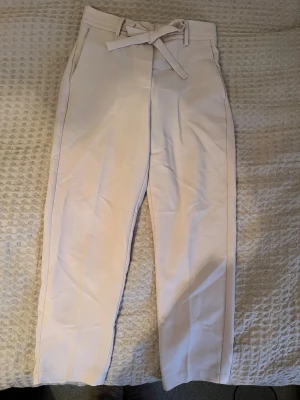 Ljusrosa kostymbyxor med knytband - Snygga ljusrosa kostymbyxor med hög midja och knytband i midjan. Byxorna har raka ben, fickor fram och diskreta bakfickor. De ger en clean och fräsch look - perfekt för dig som gillar stilrena och enkla plagg. Har klippt bort lappen, men tror den var från Mango - den var strl XS.