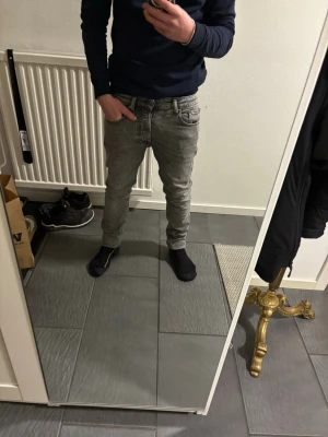 Grå skinny jeans från YPS, 30/32 - Säljer ett par grå jeans från YPS i storlek 30/32. De har en skinny passform med klassisk femficksdesign och snygga detaljer vid fickor och midja. Jeansen är tillverkade i jeansmaterial och har en modern, smal siluett som sitter tajt längs benen.