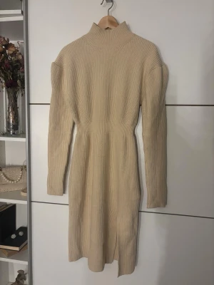 Beige stickad långklänning Adoore - Säljer en beige stickad långklänning från Adoore i storlek 38. Klänningen har ribbad struktur, polokrage, långa ärmar och en snygg slits framtill. Perfekt för dig som gillar stilrena och mysiga plagg med lite extra edge.